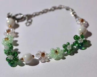May include: A delicate bracelet made with green, white, and gold beads, featuring a flower design. The bracelet has a silver clasp.