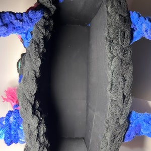 May include: A black crocheted tote bag with blue and pink yarn accents. The bag has a black fabric lining.