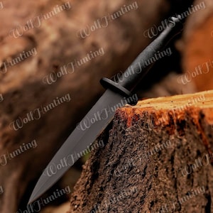 May include: A black knife with a black handle and a sharp blade. The knife is resting on a wooden stump.