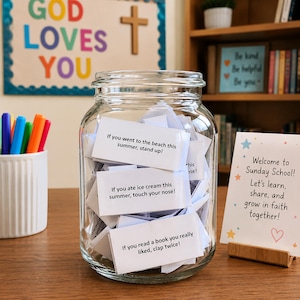 May include: A clear glass jar filled with white paper slips featuring printed prompts such as If you went to the beach this summer, stand up!, If you ate ice cream this summer, touch your nose!, and If you read a book you really liked, clap twice!