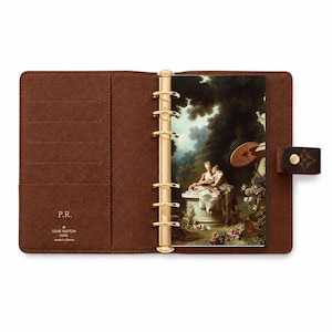 May include: A brown leather agenda planner with a gold six-ring binder mechanism. The interior features card slots, the embossed text P.R., and the Louis Vuitton Paris made in France logo. A classic painting of a couple is inserted in the rings.