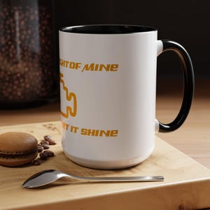 May include: White ceramic mug with a black rim and handle. The mug has a yellow check engine light icon and the text "Light of Mine Let It Shine".