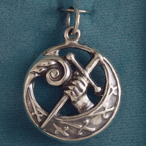 May include: A silver pendant featuring a hand holding a sword, surrounded by a circular design with a stylized wave and other swords.