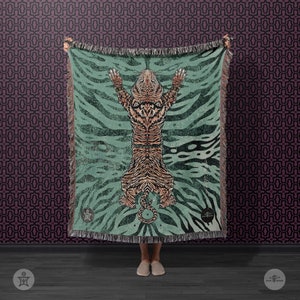 May include: A teal woven throw blanket with a tiger design. The tiger is orange and black with a white belly. The blanket has a fringe border.