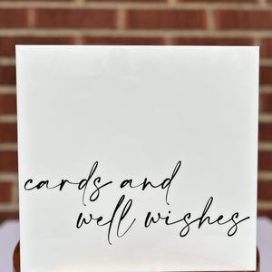 May include: White acrylic sign with black calligraphy that reads "cards and well wishes".