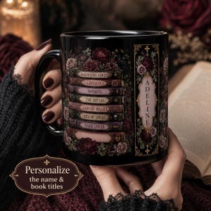 Op de afbeelding: Een zwarte keramische mok met een stapel geïllustreerde boeken met de titels Haunting Adelin, Credence, Hooked, The Ritual, God of Malice, Den of Vipers en Dark Lover, omringd door donkere bloemmotieven en een verticaal paneel met de naam Adeline.