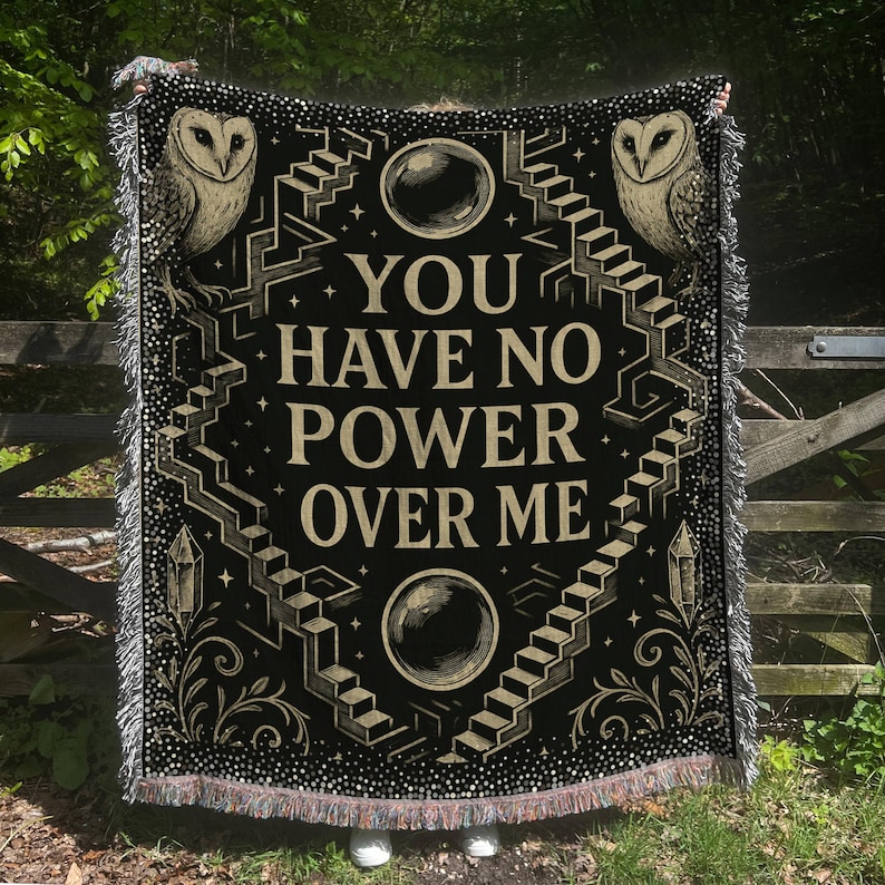 May include: Black woven throw blanket with the text "YOU HAVE NO POWER OVER ME". The design includes owls, staircases, crystals, and orbs in beige and white. The blanket has a fringed edge.