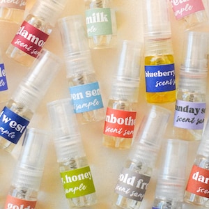 以下が含まれることがあります： カラフルなラベルが付いた、小さな透明スプレーボトルのコレクションです。「glamor」、「blueberry」、「honey」などの様々な香りの名前がラベルに表示されています。ボトルには様々な色の液体が入っており、様々な香りを連想させます。