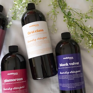 May include: Multiple dark bottles of laundry detergent with black caps. The labels read "First Class", "Glamorous", and "Black Velvet". Each bottle contains 946 ml of detergent.