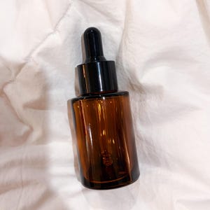 May include: A brown glass dropper bottle with a black cap and dropper. The bottle is rectangular with rounded edges. The dropper is made of black plastic. The bottle is filled with a clear liquid.