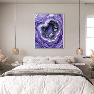 Peut inclure: Une géode d'agate violette et blanche avec un centre violet foncé. La géode est encadrée et accrochée au mur au-dessus d'un lit blanc avec une couverture grise et blanche.