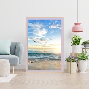 May include: A framed photograph of a beach scene with blue sky, white clouds, and a few seagulls flying overhead. The beach is sandy with a few seashells scattered on the shore. The ocean is blue and the waves are crashing on the shore.