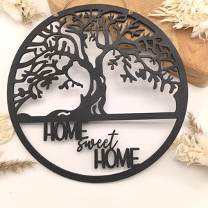 Może przedstawiać: Okrągły drewniany znak w kolorze czarnym z wzorem drzewa życia i napisem "Home Sweet Home" w ozdobnym kroju pisma.