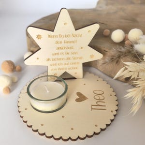 May include: Wooden star-shaped candle holder with a small glass votive candle holder and the text "Wenn Du bei Nacht den Himmel anschaust wird es Dir sein als lachten alle Sterne. weil ich auf einem von ihnen wohne" and the name "Theo" below.