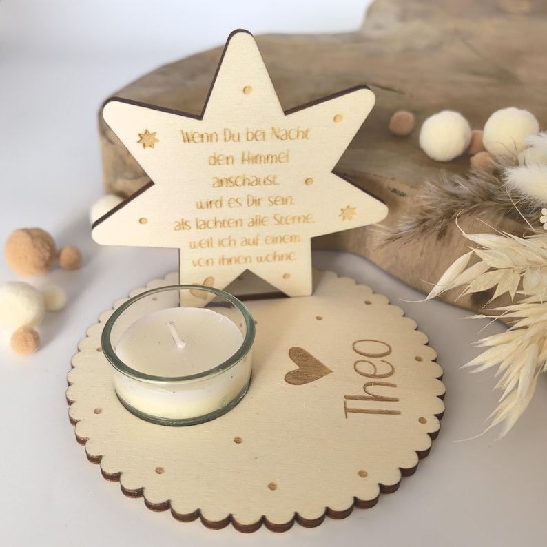 May include: Wooden star-shaped candle holder with a small glass votive candle holder and the text "Wenn Du bei Nacht den Himmel anschaust wird es Dir sein als lachten alle Sterne. weil ich auf einem von ihnen wohne" and the name "Theo" below.