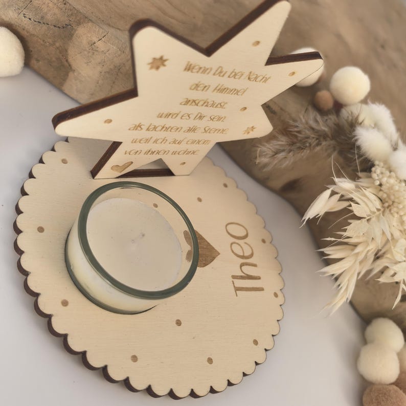 May include: Wooden star-shaped candle holder with the text "Wenn Du bei Nacht den Himmel anschaust wird es Dir sein als lachten alle Sterne weil ich auf eines von ihnen wohne" and the name "Theo" engraved on the base.