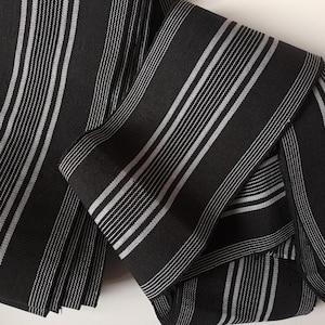 May include: Black and white striped fabric with a woven texture. The fabric is folded and layered, showing the pattern.