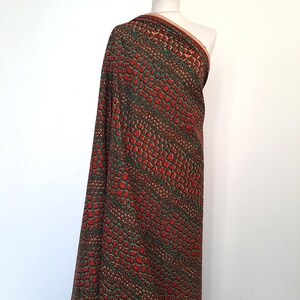 May include: Red and green fabric with a snakeskin pattern. The fabric is draped over a mannequin.