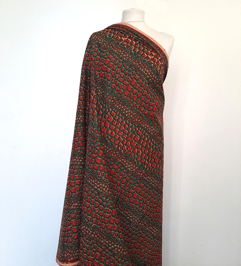 May include: Red and green fabric with a snakeskin pattern. The fabric is draped over a mannequin.