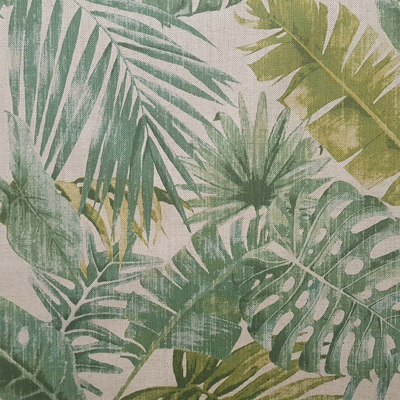 May include: A fabric with a green and white tropical leaf pattern. The leaves are stylized and have a vintage look.