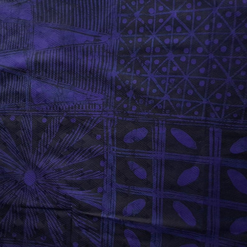 May include: A close-up of a textile with a repeating pattern in shades of dark blue and black. The design features geometric shapes, including triangles, circles, and lines, creating a textured appearance. The fabric appears to be soft and possibly silk.