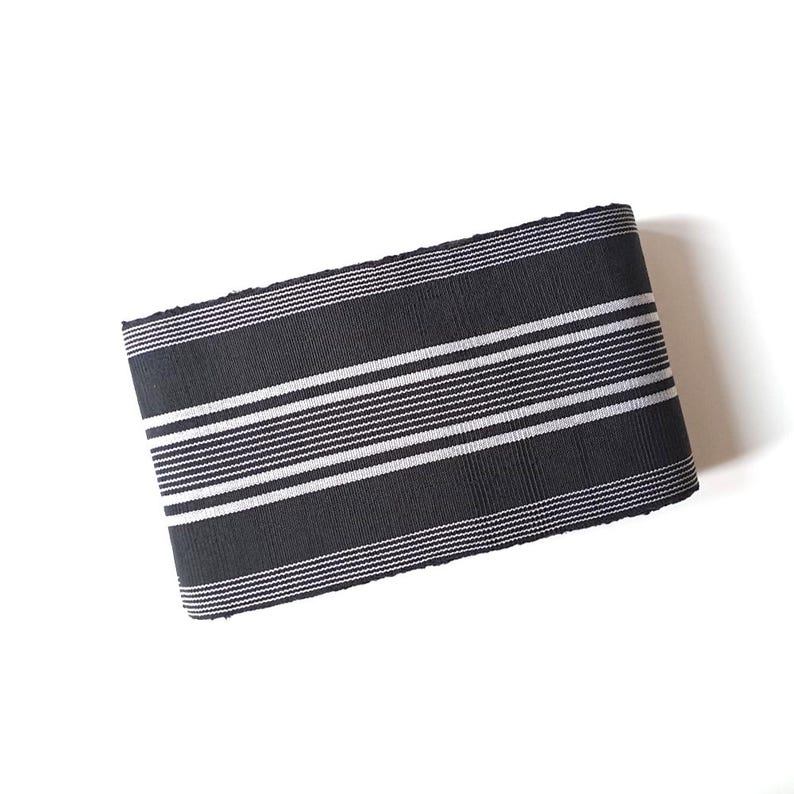 May include: Black and white striped fabric with a woven texture. The fabric is folded in half and has a slightly frayed edge.