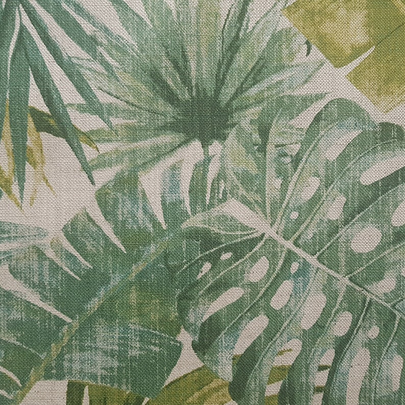 May include: A close-up of a fabric with a green and white tropical leaf pattern. The fabric has a textured, linen-like appearance.