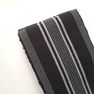 May include: Black and white striped fabric with a woven texture. The fabric is folded in half and the stripes are running vertically.