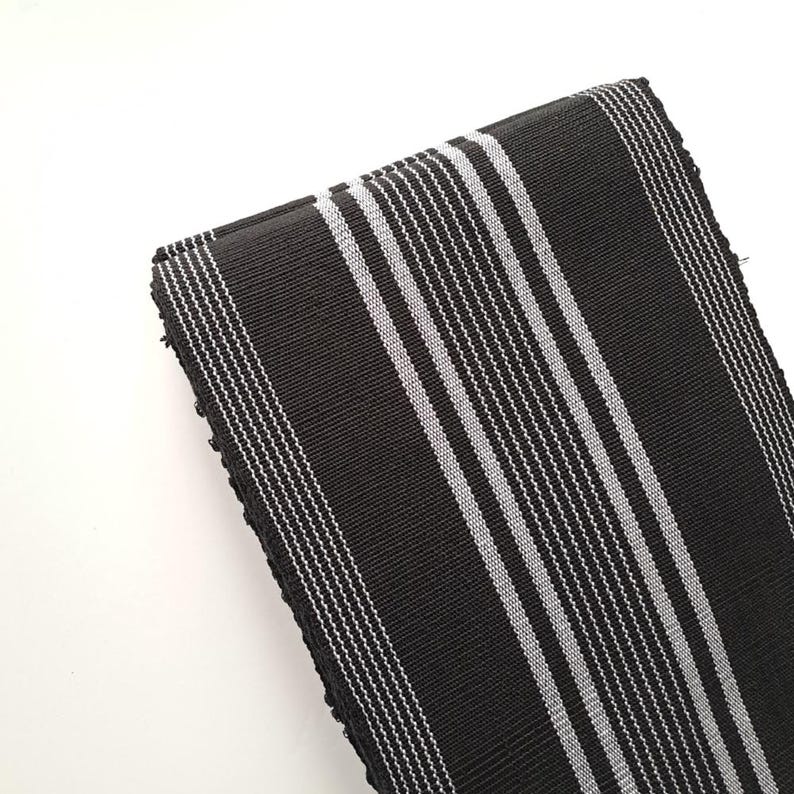 May include: Black and white striped fabric with a woven texture. The fabric is folded in half and the stripes are running vertically.