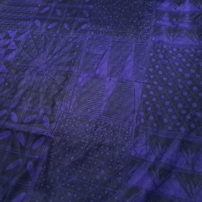 May include: A close-up of a textile with a patchwork design. The fabric features a dark blue and purple color scheme. The design includes geometric shapes, such as triangles, circles, and lines, creating a textured appearance. The overall pattern is intricate and detailed.