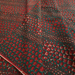 May include: Red and teal fabric with a repeating pattern of small, overlapping circles. The fabric has a subtle sheen and a soft texture.