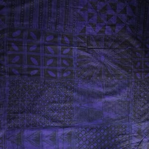 May include: A close-up of a textile with a geometric pattern in shades of purple and black. The design features squares, triangles, and sunburst shapes. The fabric has a textured appearance.