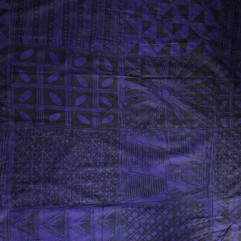 May include: A close-up of a textile with a geometric pattern in shades of purple and black. The design features squares, triangles, and sunburst shapes. The fabric has a textured appearance.
