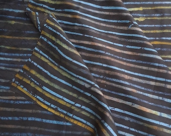 May include: Dark fabric with horizontal stripes in shades of blue, yellow, and tan. The stripes have a slightly distressed appearance, creating a textured effect. The fabric is folded, showing the pattern from different angles.