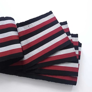 May include: Red, black and grey striped fabric ribbon. The ribbon is folded in a stack of four layers.