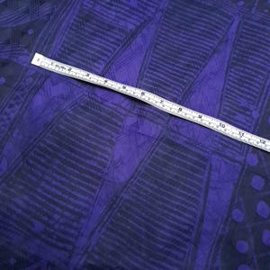 May include: A piece of fabric with a geometric pattern in shades of purple and navy blue. The pattern includes lines and shapes. A ruler is placed across the fabric, showing measurements up to 12 inches.