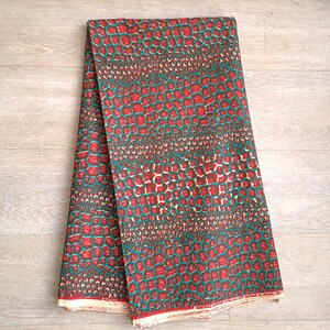 May include: Red and green fabric with a repeating pattern of small circles. The fabric is folded in half and the edges are visible. The fabric is made of cotton and is suitable for sewing projects.