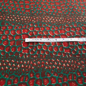 May include: Red and green fabric with a repeating pattern of small, rounded shapes. The fabric is measured with a ruler, showing 7 inches.
