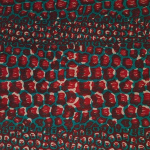 May include: A fabric with a repeating pattern of red and teal shapes resembling animal skin. The fabric has a textured surface.