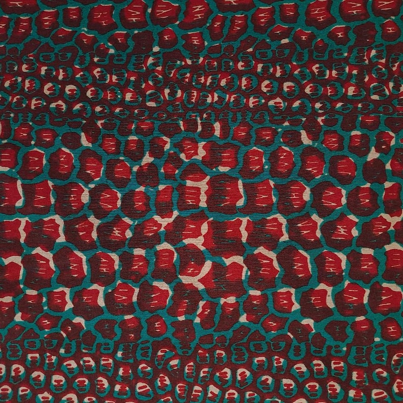 May include: A fabric with a repeating pattern of red and teal shapes resembling animal skin. The fabric has a textured surface.