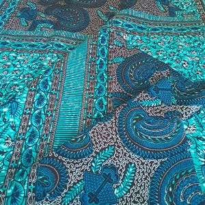 May include: A folded textile with a vibrant teal, blue, and brown pattern. The design features intricate paisley and floral motifs, with a central striped border. The fabric has a detailed, ornate appearance, suitable for various craft projects.