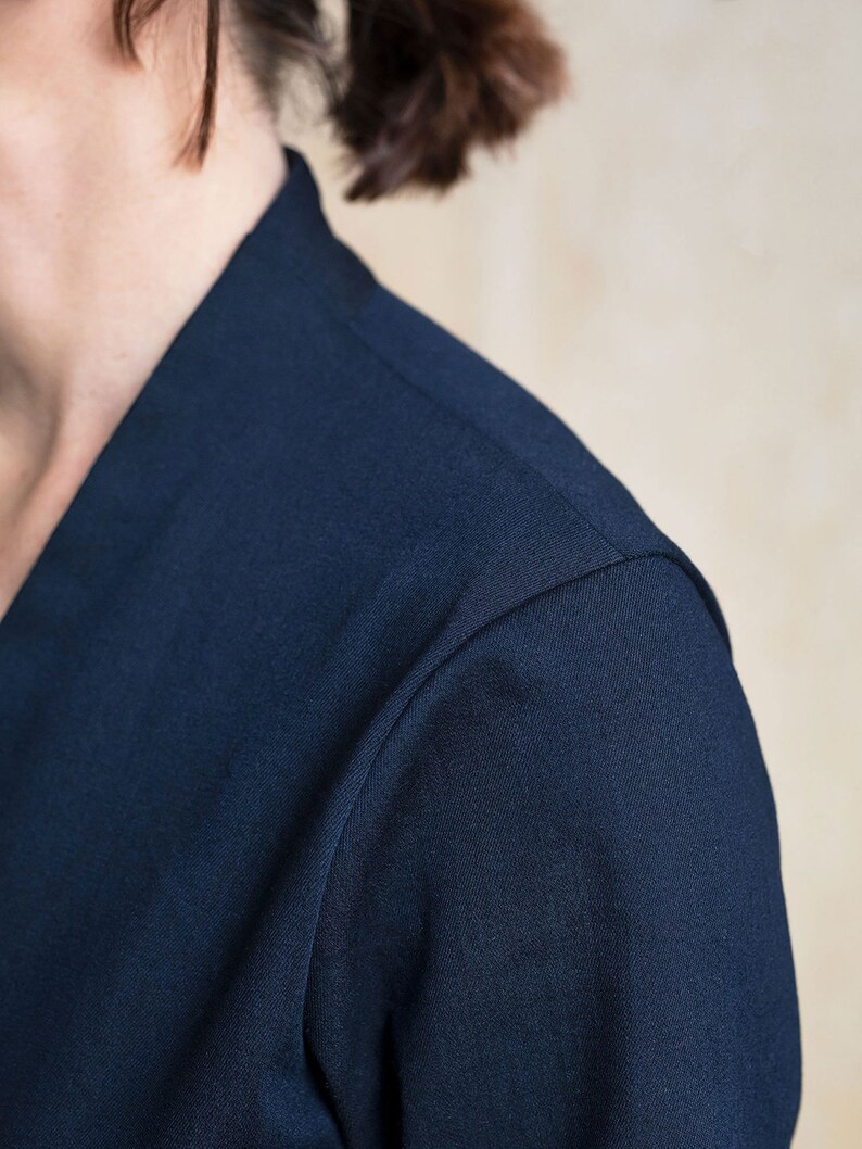 May include: Close-up of the shoulder seam of a navy blue shirt. The fabric is smooth and has a subtle texture.
