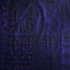 May include: A close-up of a fabric with a repeating geometric pattern in shades of dark blue and black. The design includes squares, triangles, and circular shapes, creating a textured appearance. The fabric has a slightly wrinkled texture.