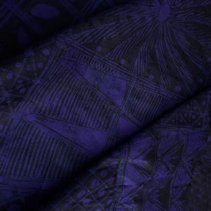 May include: Close-up of a folded fabric with a dark purple and black geometric pattern. The design includes lines, dots, and shapes, creating a textured appearance. The fabric has a slight sheen, suggesting a smooth material.