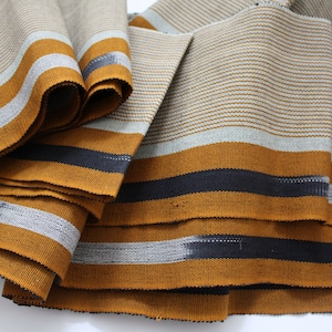 May include: Close-up of a stack of fabric with a striped pattern in shades of gray, yellow, and black.