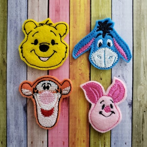 May include: Four felt appliques of Winnie the Pooh characters: a yellow bear, a blue donkey, an orange tiger, and a pink pig. Each applique has embroidered facial features.