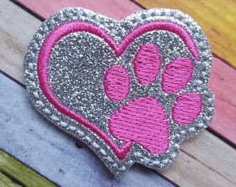 May include: A silver glitter heart with a pink paw print inside. The heart is outlined with a silver stitching.