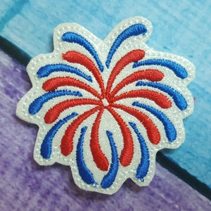 May include: A white felt patch with a red and blue embroidered firework design. The firework is a stylized design with a burst of red and blue flames.