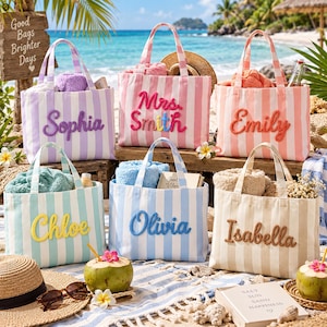 Pode incluir: Seis sacolas de lona listradas com nomes bordados em várias cores. As bolsas estão expostas em uma praia, cada uma contendo toalhas ou itens. Os nomes incluem Sophia, Mrs. Smith, Emily, Chloe, Olivia e Isabella. Uma placa de madeira diz Good Bags Brighter Days.