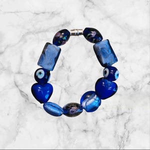 May include: A blue and silver bracelet with various charms, including hearts, evil eyes, and square beads.